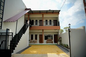 A two-story building with a staircase leading to the entrance, a balcony on the upper floor, and a paved courtyard.