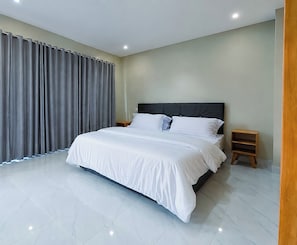 A modern bedroom with a large bed, grey curtains, and a wooden nightstand.