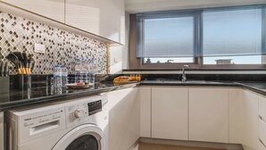 Cocina pequeña equipada con lavadora, un lavabo y una ventana con persianas.