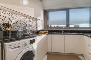 Cocina pequeña equipada con lavadora, un lavabo y una ventana con persianas.