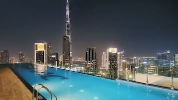 A swimming pool with a city skyline view at night, including a prominent skyscraper.