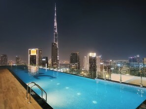 Una piscina con vista al horizonte urbano nocturno, incluyendo un rascacielos destacado.