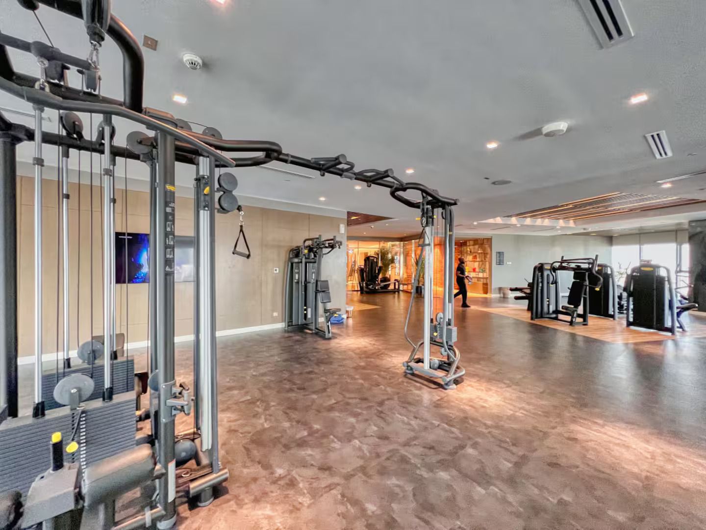 Et rummeligt fitnesscenter med diverse træningsmaskiner, et stort spejl og et fjernsyn på væggen.