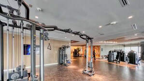 Un gimnasio amplio con diversas máquinas de ejercicio, un espejo grande y un televisor en la pared.