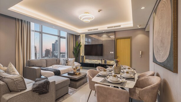 Una sala de estar moderna con un sofá, una mesa de comedor lista para cuatro personas y un televisor de pantalla plana montado en la pared.