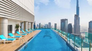 Piscina infinita en la azotea con sillones de descanso y vista al horizonte urbano.
