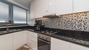 Una cocina moderna con armarios blancos, encimera negra, pileta de acero inoxidable y estufa negra.