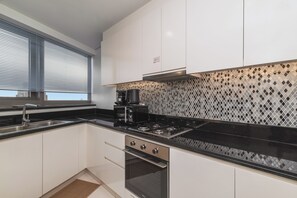 Una cocina moderna con armarios blancos, encimera negra, pileta de acero inoxidable y estufa negra.