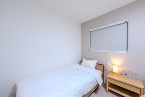 A single bed with a wooden headboard, a bedside table with a lamp, and a window with a blind. - Nikyo HARANAGI Villa Osaka (Osaka)