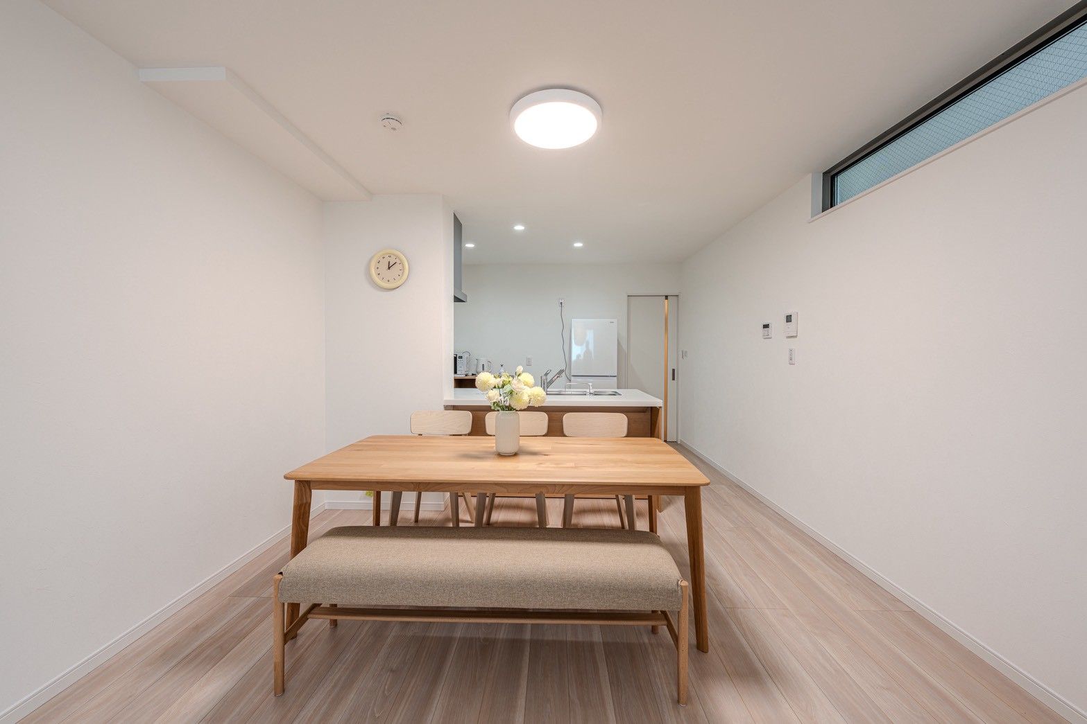 A modern dining area with a wooden table, bench, and a vase of flowers.