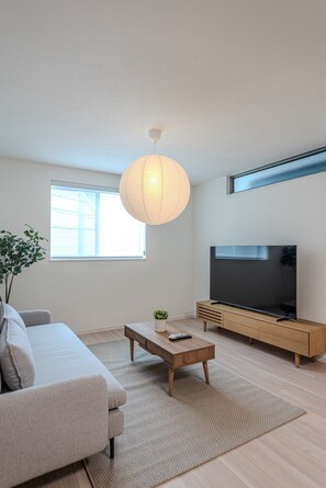 A modern living room with a sofa, coffee table, TV, and a hanging light fixture. - Nikyo HARANAGI Villa Osaka (Osaka)