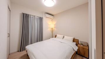 A hotel room with a bed, bedside table, lamp, air conditioning unit, and curtains.
