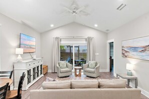 A spacious living room with a high ceiling, a ceiling fan, a large window with curtains, a beige sofa, two armchairs, a small round table, and a cabinet with glass doors. - Coastal Getaway in Perdido Key (Pensacola)