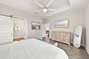 A bedroom with a bed, a dresser, a ceiling fan, and artwork on the walls.