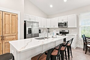 A modern kitchen with white cabinetry, stainless steel appliances, a marble countertop, and a dining area with bar stools.