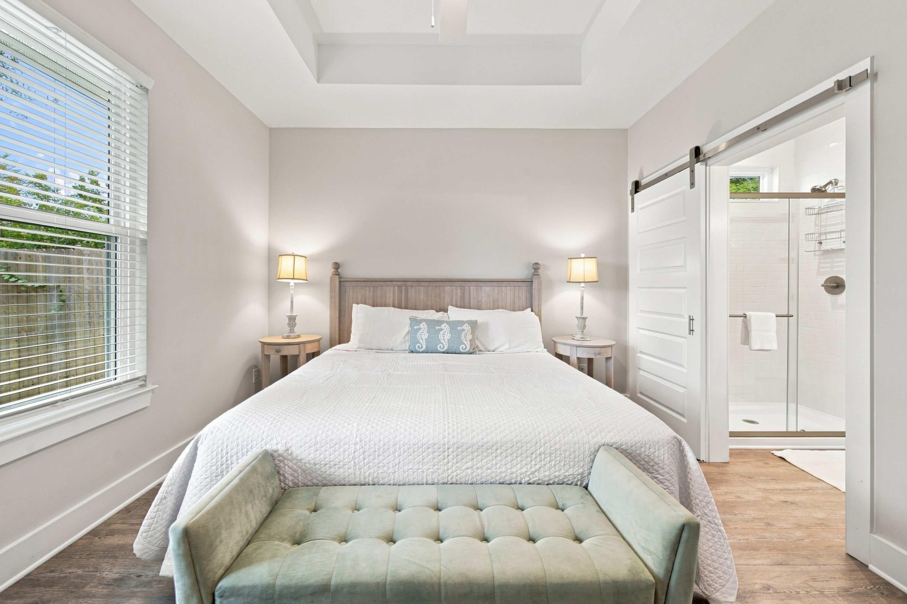 Een slaapkamer met een groot bed, nachtlampjes, een bankje en een schuifdeur naar een badkamer.