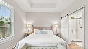 A bedroom with a large bed, bedside lamps, a bench, and a sliding door leading to a bathroom. - Coastal Getaway in Perdido Key (Pensacola)