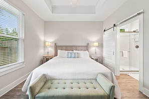 Quarto com uma cama grande, luminárias laterais, um banco e uma porta deslizante que dá para um banheiro.