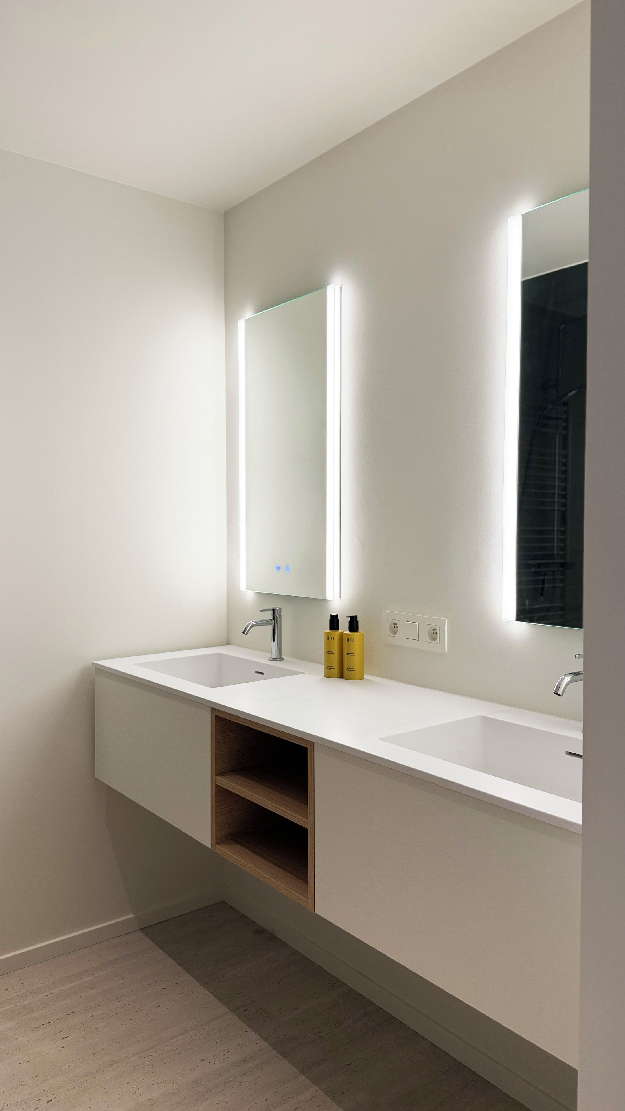 A modern bathroom with two sinks, a mirror, and built-in shelves.