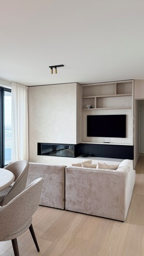 Ein modernes Wohnzimmer mit Fernseher, einer Couch und einem Essbereich mit Stühlen.