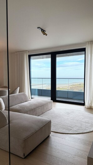 Ein modernes Wohnzimmer mit großem Fenster, einer Couch und Blick auf den Strand.