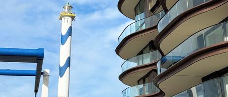 A modern building with a curved balcony design and a lighthouse in the background.