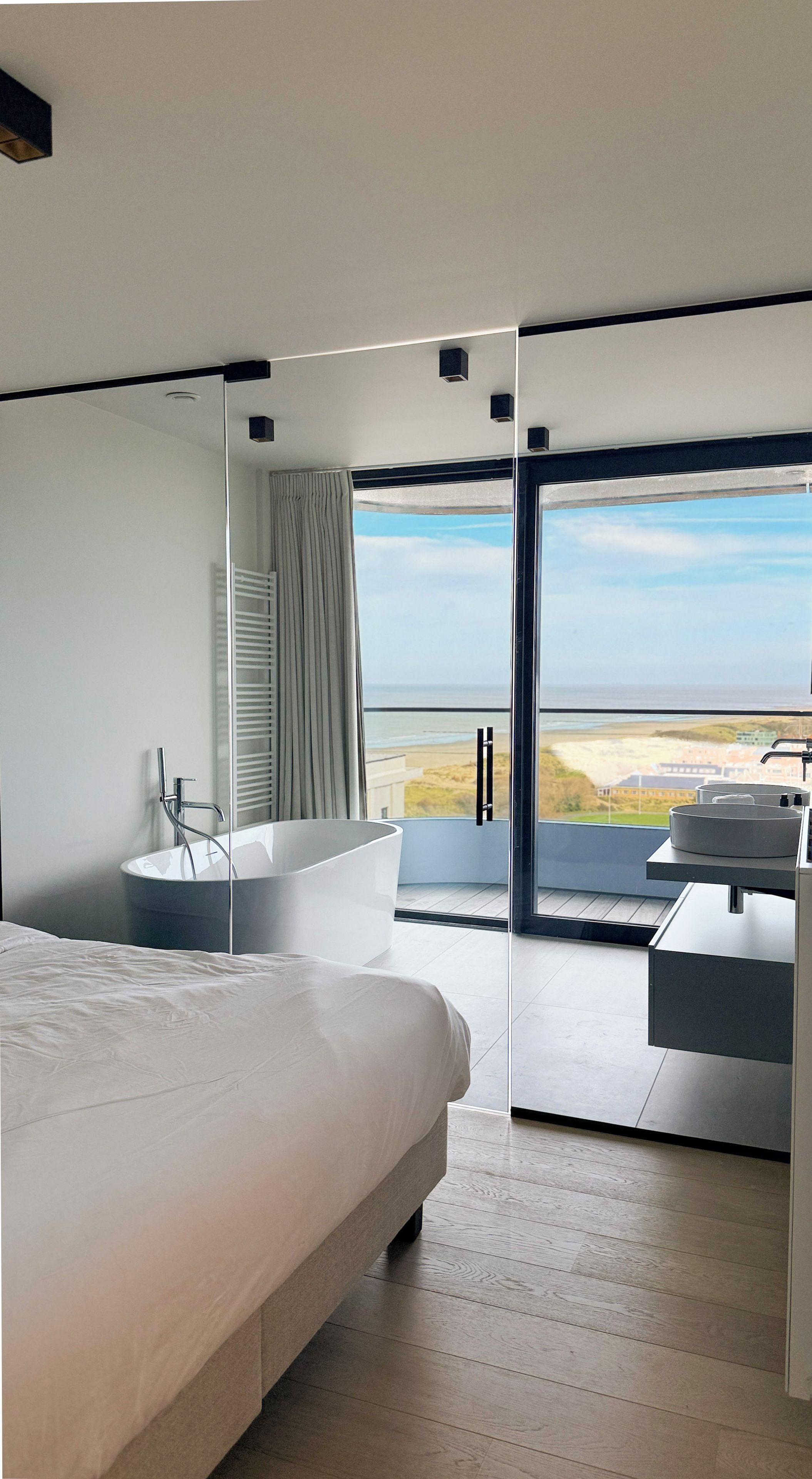 Een moderne slaapkamer met een groot bed, een badkuip en een balkon met uitzicht op het strand.