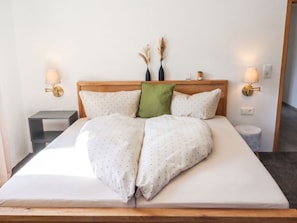 Una cama bien hecha con cabecera de madera, dos mesitas de noche y lámparas de pared.