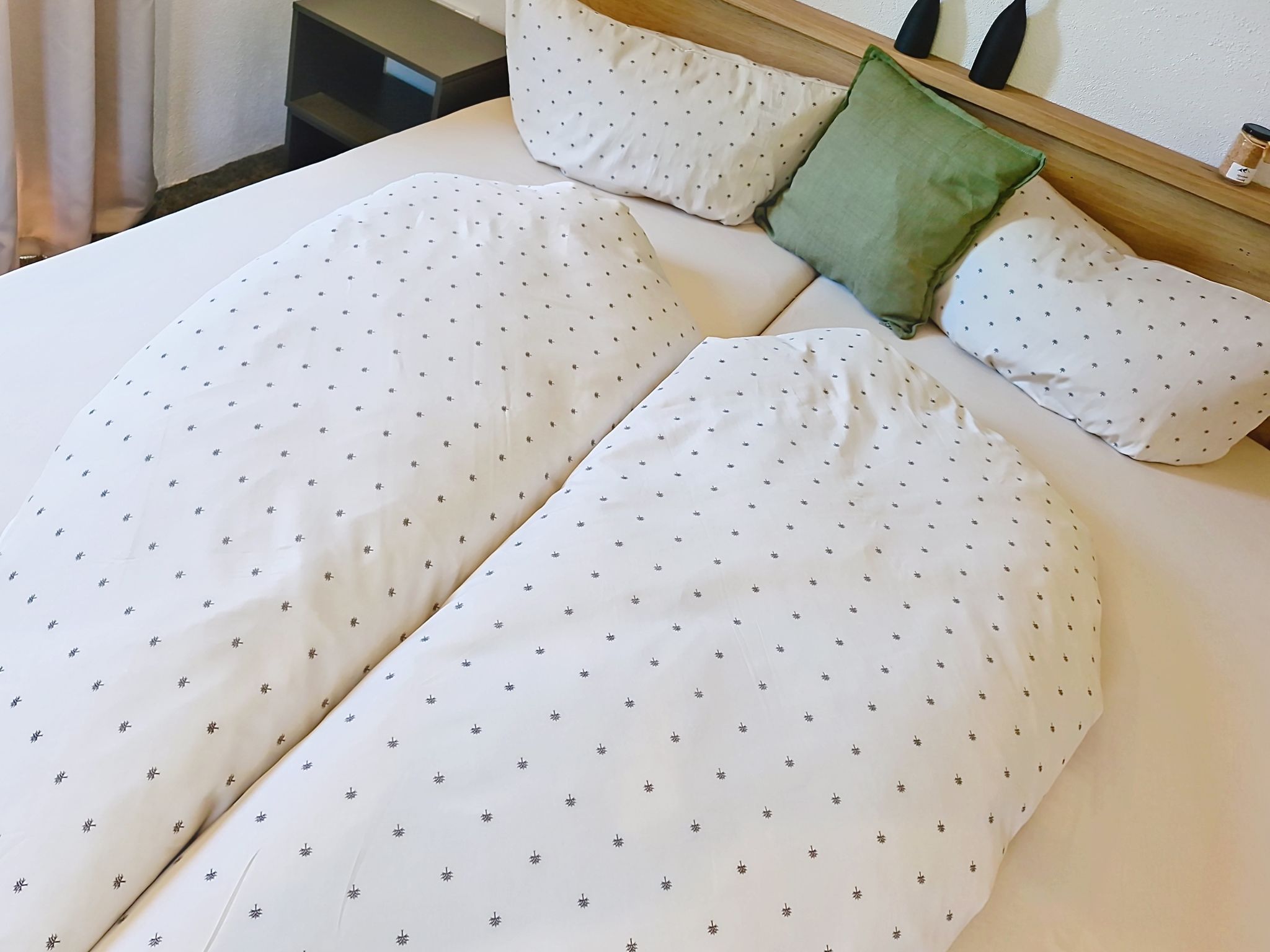 A neatly made bed with white sheets and a green pillow.