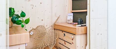A wooden bathroom with a shelf holding a plant, a woven basket, and a box of floor cleaner.