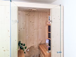 Una sauna de madera con puerta, panel de control, un botón rojo y una planta.