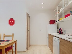 A compact kitchen with a wooden table and chairs, a red appliance, and a wall-mounted shelf with glassware. - Ubytkostka by Interhome (Rokytnice nad Jizerou)