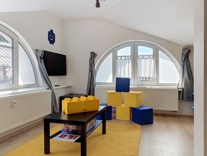 A room with a TV, a table with toys, and large windows. - Ubytkostka by Interhome (Rokytnice nad Jizerou)