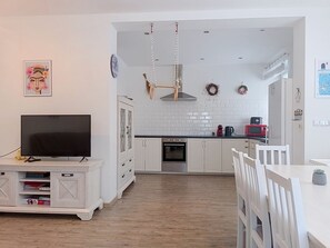 Een moderne keuken met witte kasten, een inbouwoven en een eethoek met een witte tafel en stoelen.