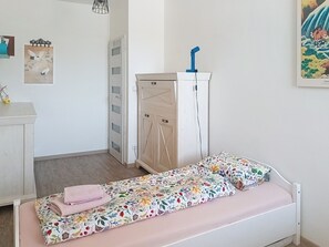 Ein kleines, ordentlich eingerichtetes Schlafzimmer mit einem Einzelbett, einem Kleiderschrank und einem Schreibtisch.