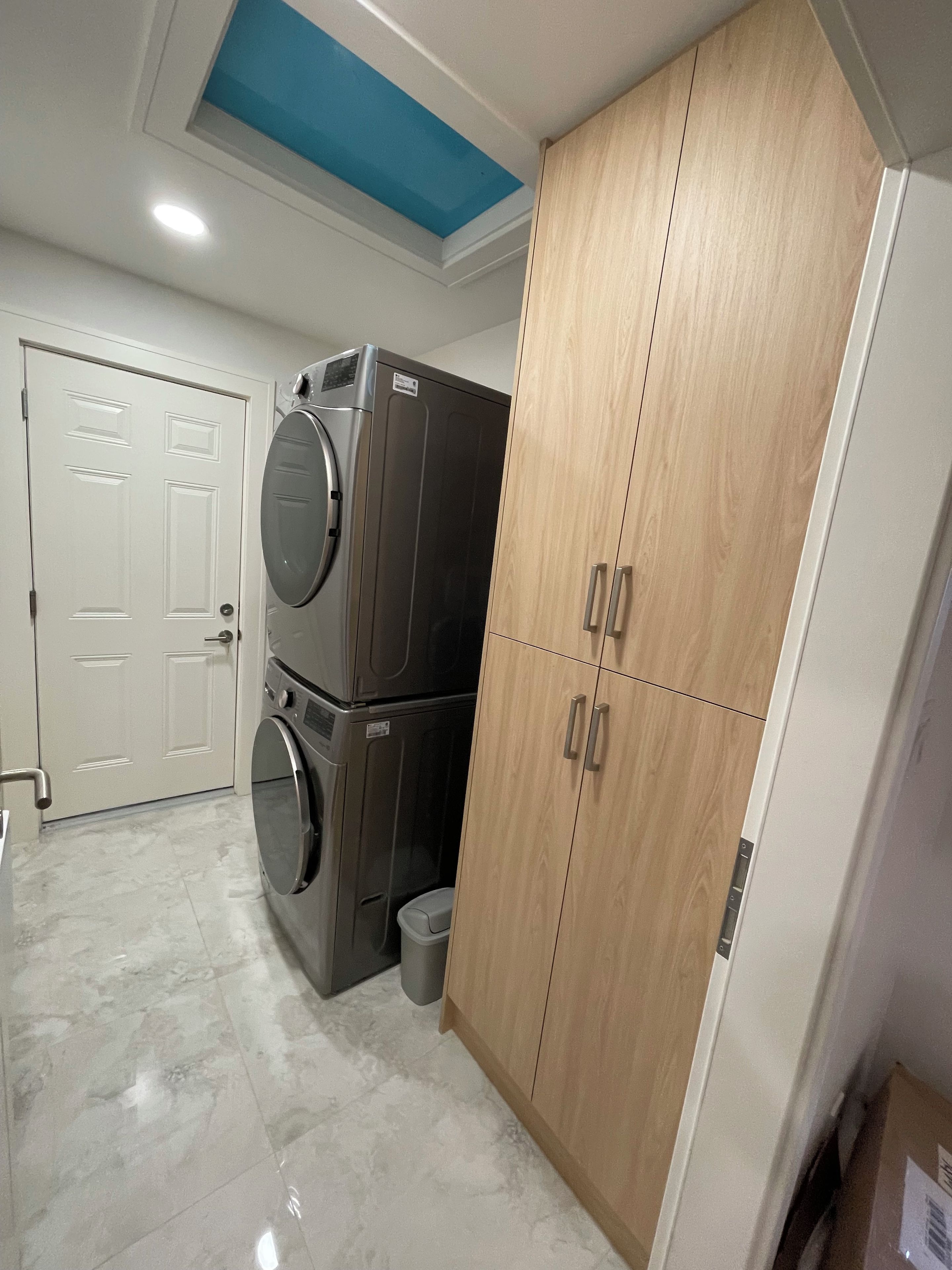 A laundry room with a stacked washer and dryer, a wooden wardrobe, and a white door.