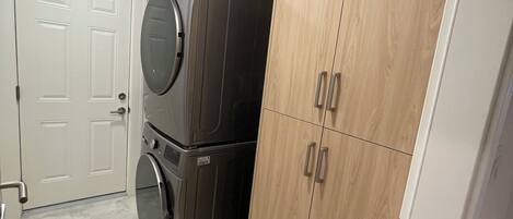 Une buanderie équipée d’un lave-linge et d’un sèche-linge superposés, d’une armoire en bois et d’une porte blanche.