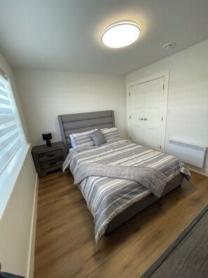 A bedroom with a bed, bedside table, and a window with blinds. - Beautiful modern home in a quiet neighbourhood in Charlottetown (Charlottetown)