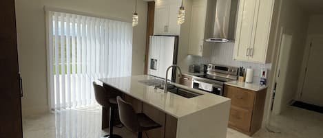Una cocina moderna con una isla central, taburetes de bar e iluminación colgante.