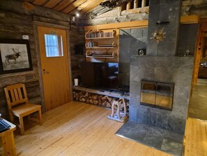A log cabin interior with a fireplace, wooden furniture, and a mounted television.