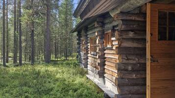 Hirsimökki, jossa on puinen terassi ja ovi, ja jonka ympärillä on metsää.