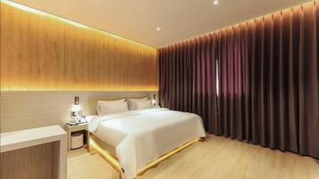 Habitación de hotel moderna con una cama grande, mesitas de noche, un cabecero de madera y vistas de la ciudad a través de cortinas.