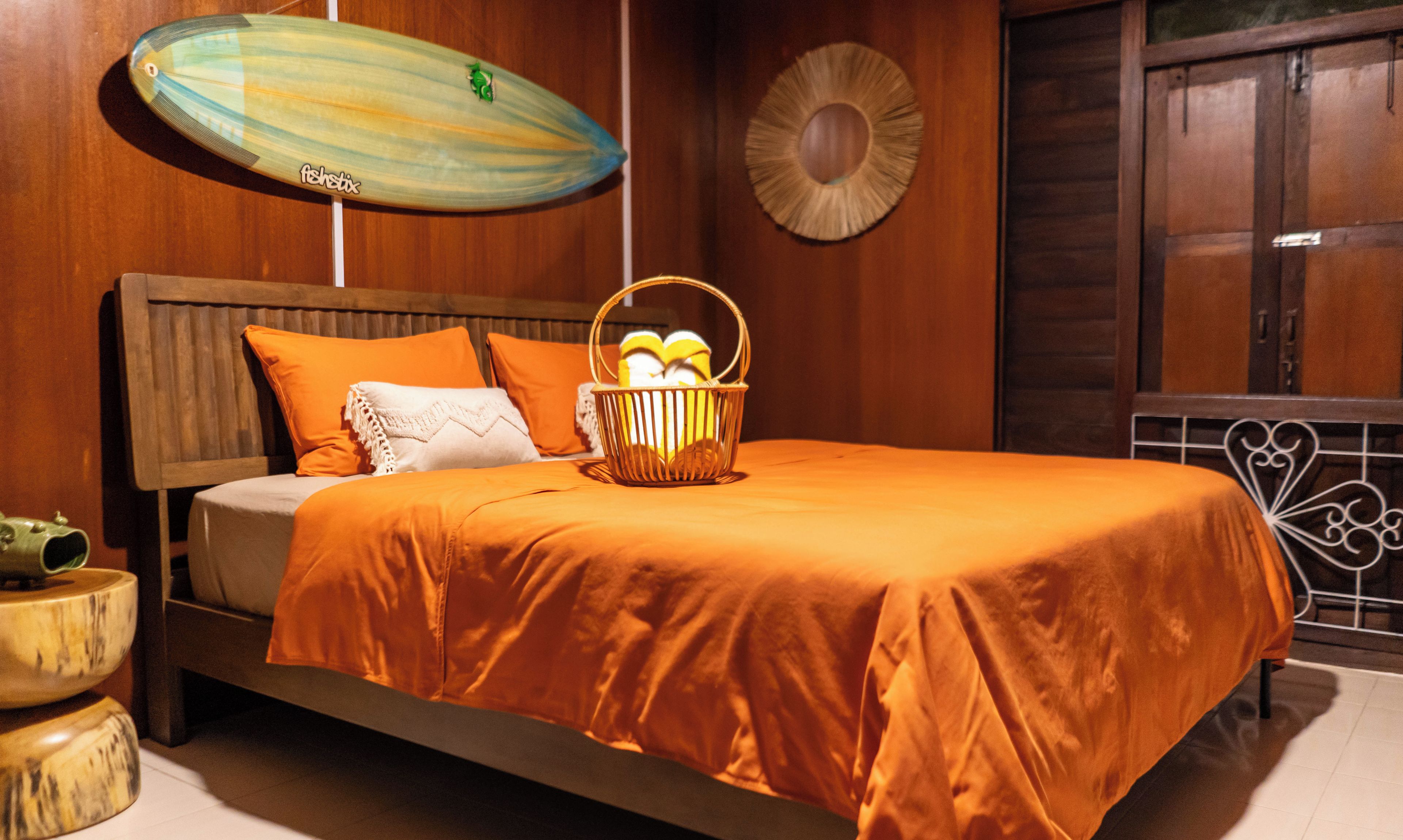 Een bed met een oranje sprei, een houten hoofdbord en een mand met fruit.