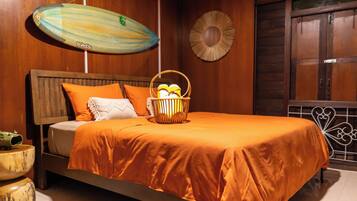 Een bed met een oranje sprei, een houten hoofdbord en een mand met fruit.