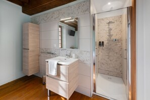 Ein modernes Badezimmer mit einem Holzlagerfläschchen, einem Spiegel, einer Dusche mit Glastür und einer gefliesten Wand.