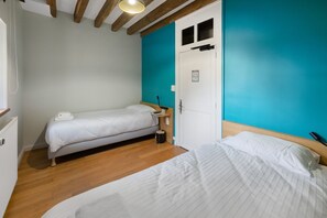 Ein Schlafzimmer mit zwei Betten, Holzboden, einer weißen Tür mit Fenster und einer blauen Wand.
