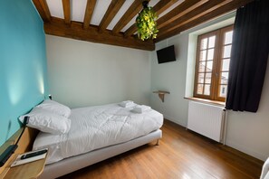 Ein Schlafzimmer mit einem Bett, einem an der Wand montierten Fernseher, einem Fenster mit Vorhängen und einer hängenden Pflanze.