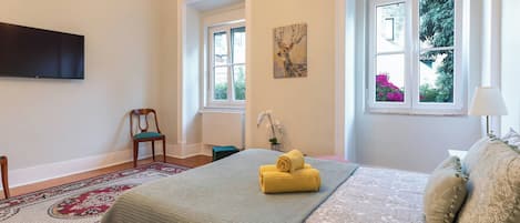 A bedroom with a bed, a chair, a TV, and two windows.