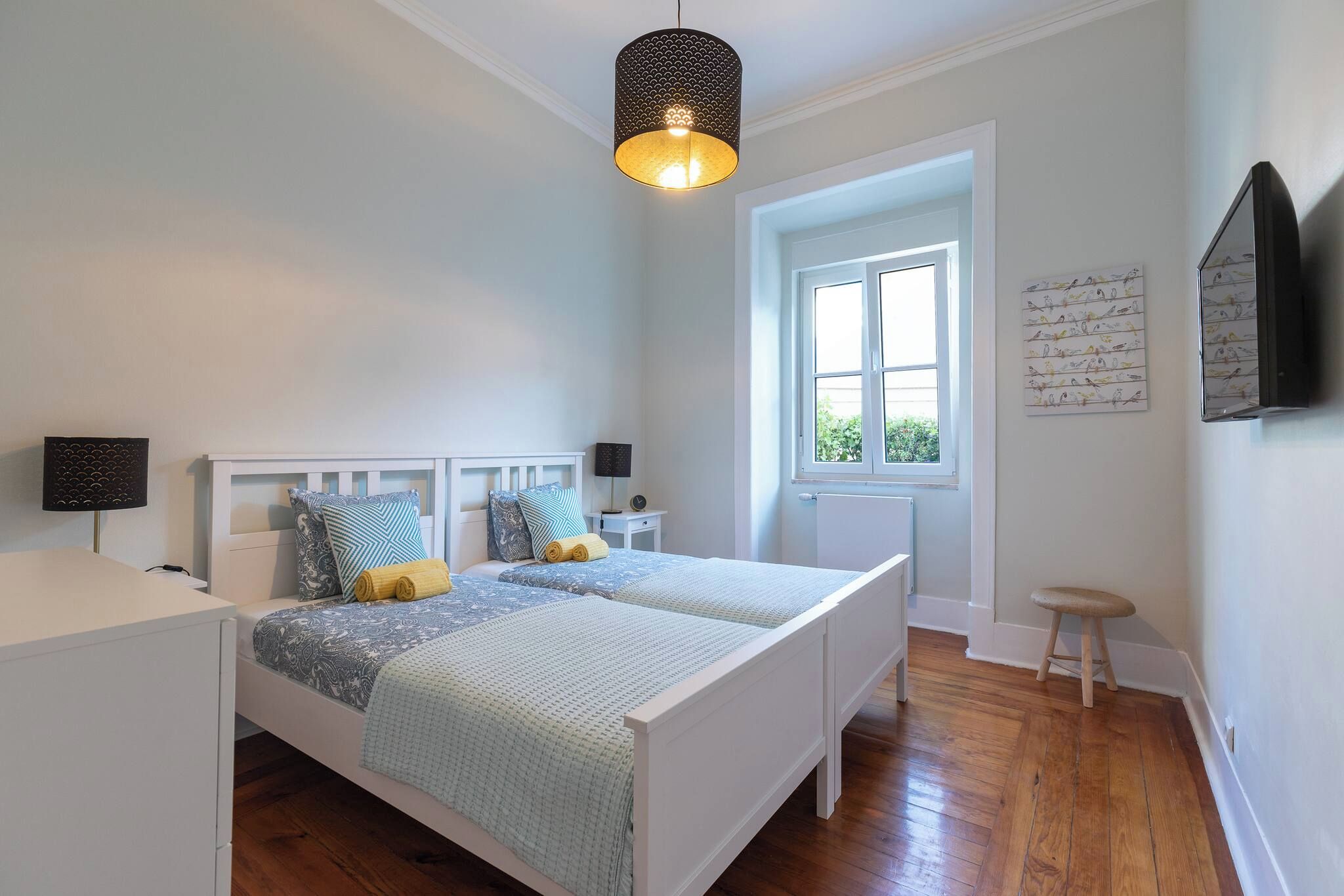 A bedroom with a double bed, bedside lamps, a window, and a wall-mounted TV.