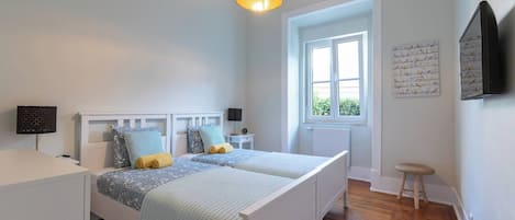 A bedroom with a double bed, bedside lamps, a window, and a wall-mounted TV.